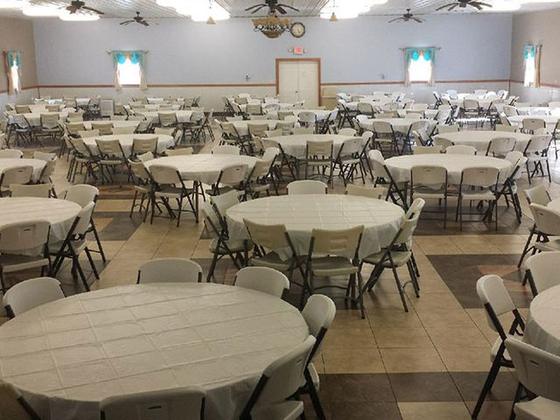 Rows of round tables with white tablecloths and folding chairs filling the banquet hall