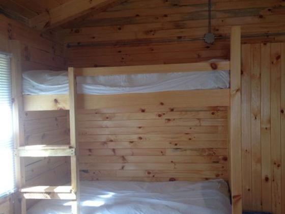 Wooden bunk beds with white mattress covers against knotty-pine walls